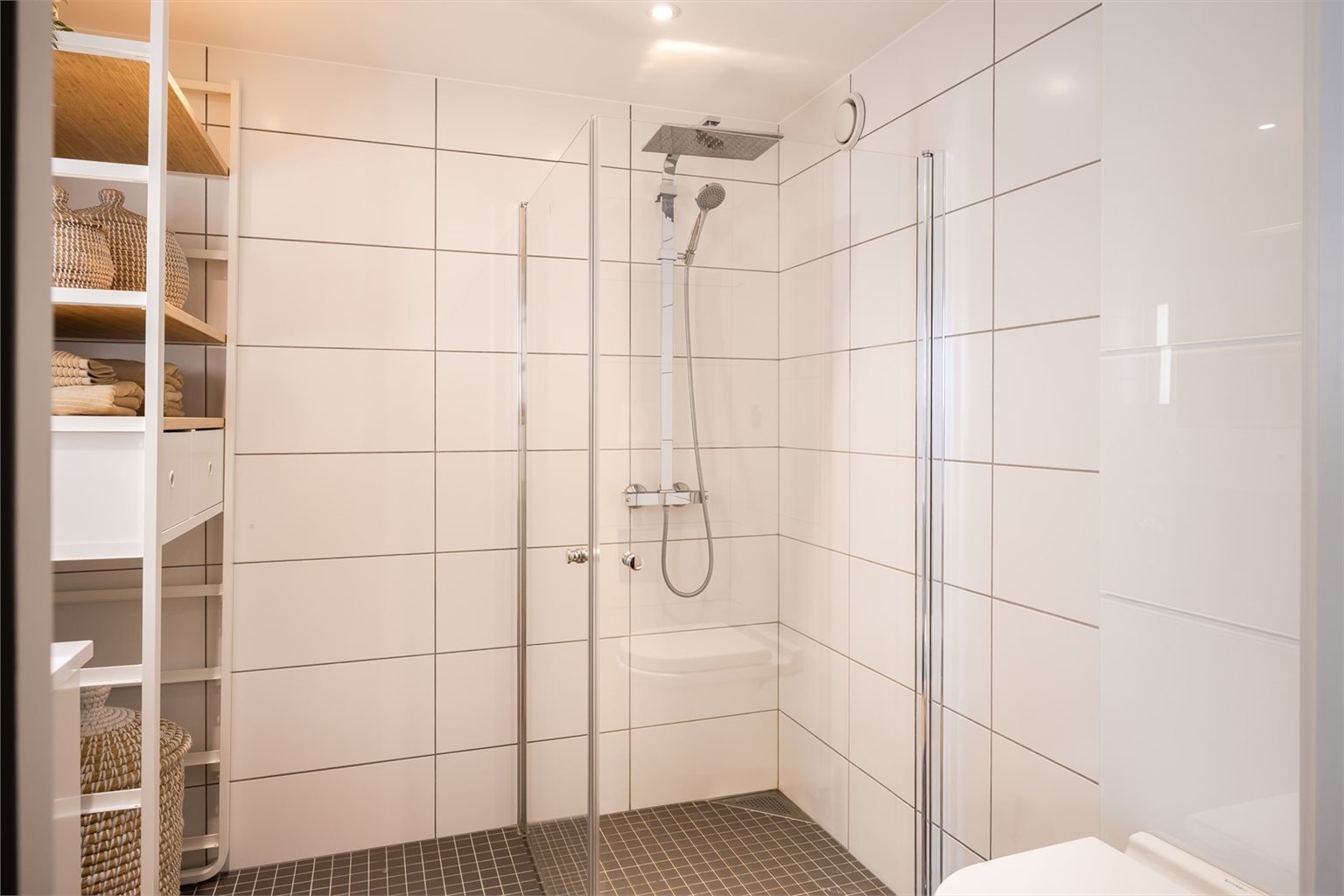 Badet har behagelig gulvvarme og er innredet med vegghengt toalett, dusjhjørne, opplegg for vaskemaskin, samt baderomsinnredning og speil med integrert belysning. 