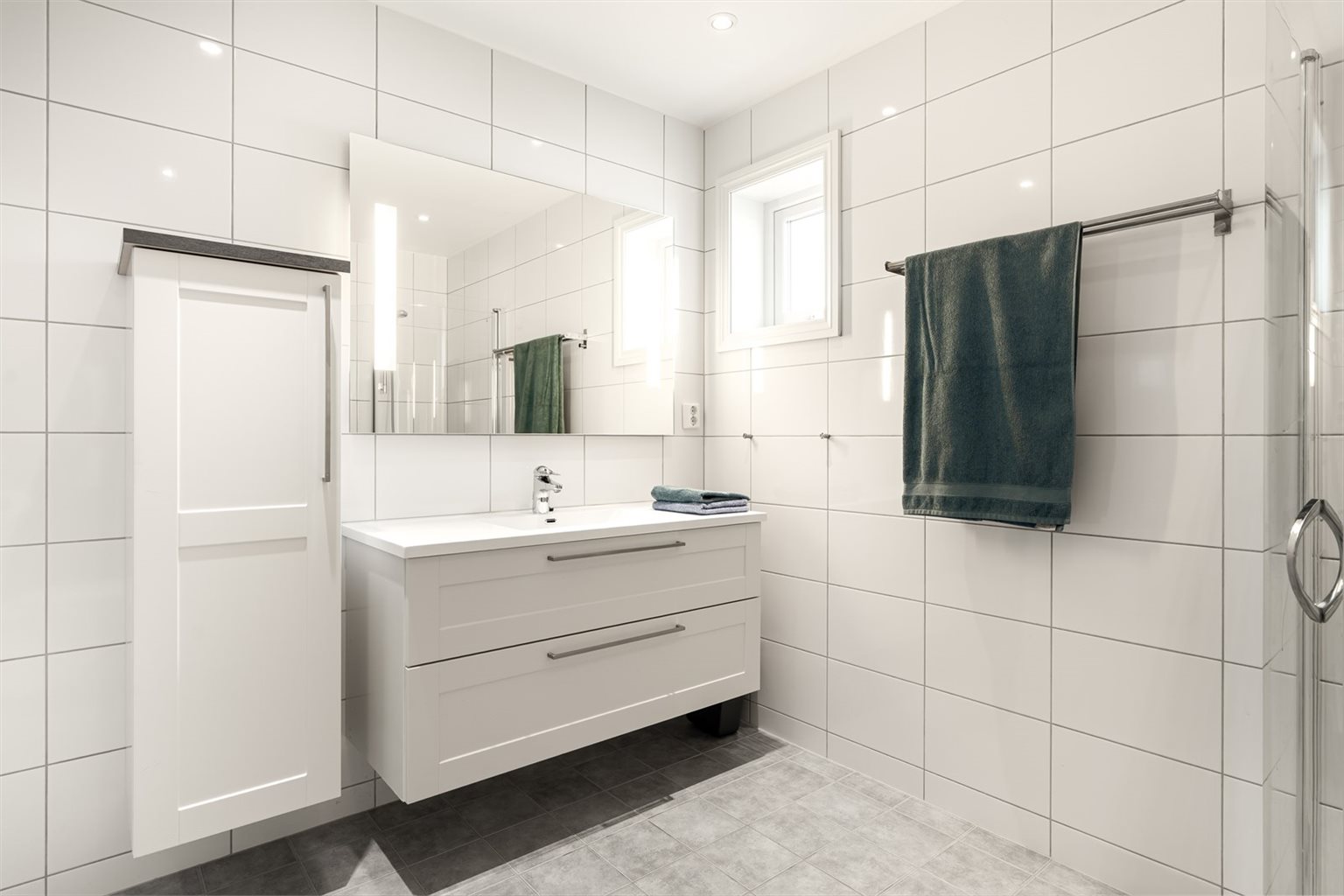 Badet i 2. etasje har flislagte overflater og er utstyrt med innfellbare dusjdører, baderomsinnredning og vegghengt toalett.