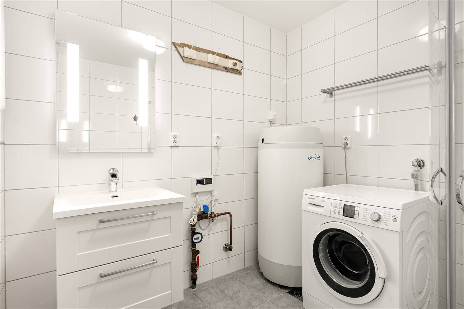Badet i 1. etasje har flislagte overflater og er utstyrt med innfellbare dusjdører, baderomsinnredning, vegghengt toalett og opplegg for vaskemaskin.