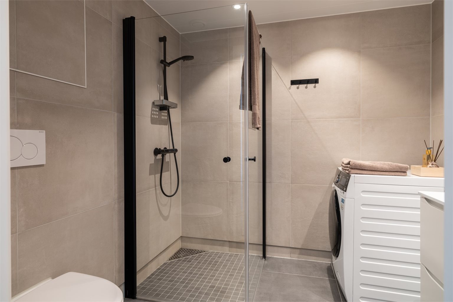 Badet byr på innfellbare dusjdører, servant, vegghengt toalett og opplegg for vaskemaskin.