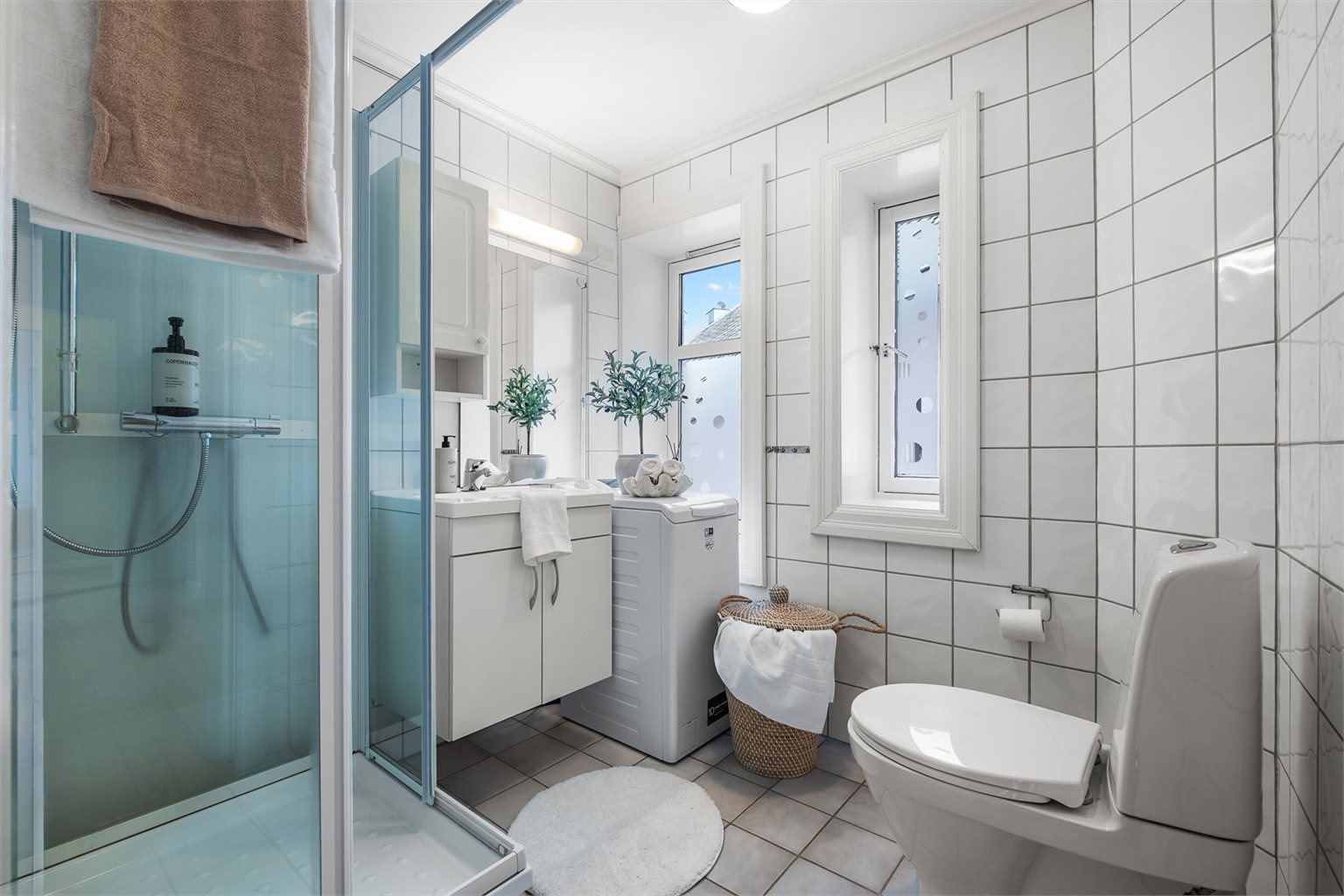Badet har en arealeffektiv løsning og er innredet med servant, toalett, dusj og opplegg for toppmatet vaskemaskin