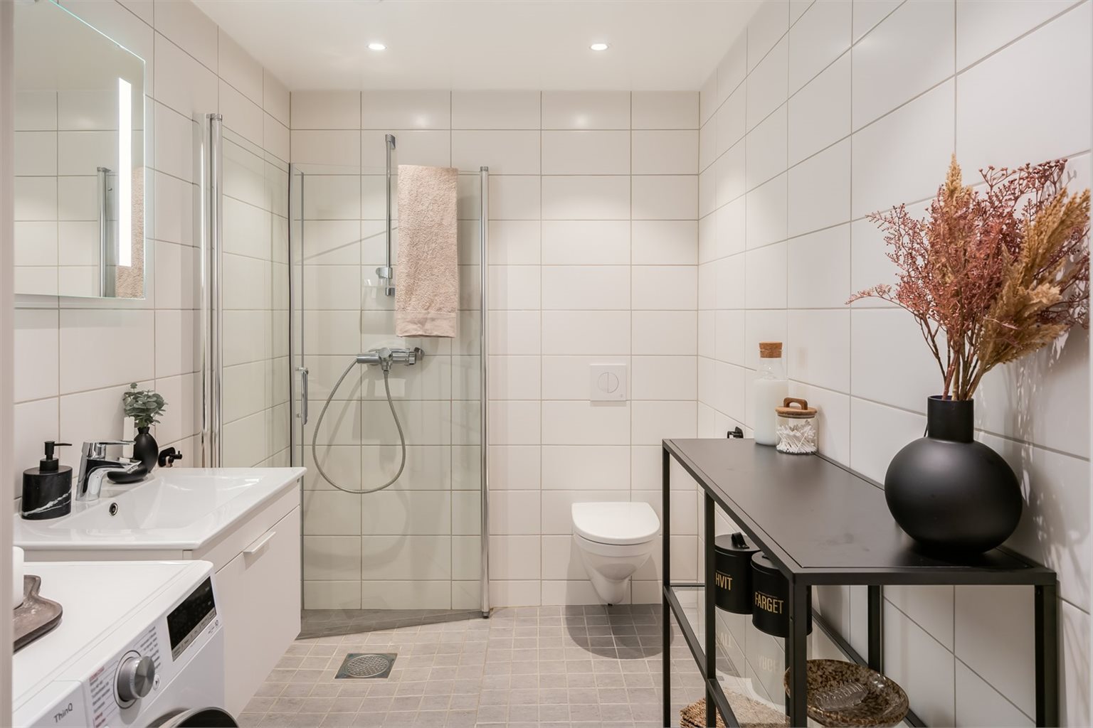 Pent og flislagt bad på 4,5m² med behagelig gulvvarme. Badet er utstyr med innfellbare dusjdører, opplegg for vaskemaskin, servant, servantskap og veggmontert wc.