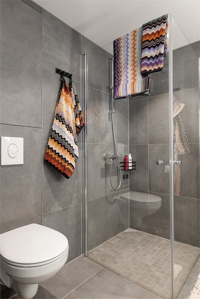 Badet har veggmontert toalett, dusjhjørne med innfellbare glassdører og spotter i taket. 