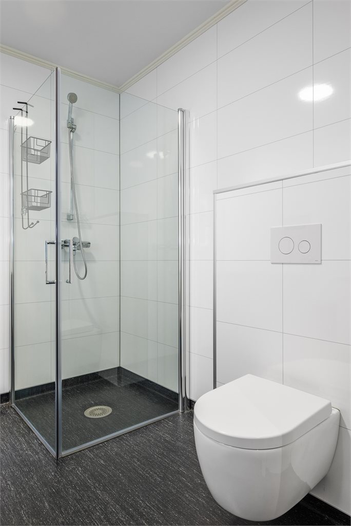 Badet er utstyrt med innfellbare dusjdører, veggmontert wc, servantskap, opplegg for vaskemaskin og mekanisk avtrekk.