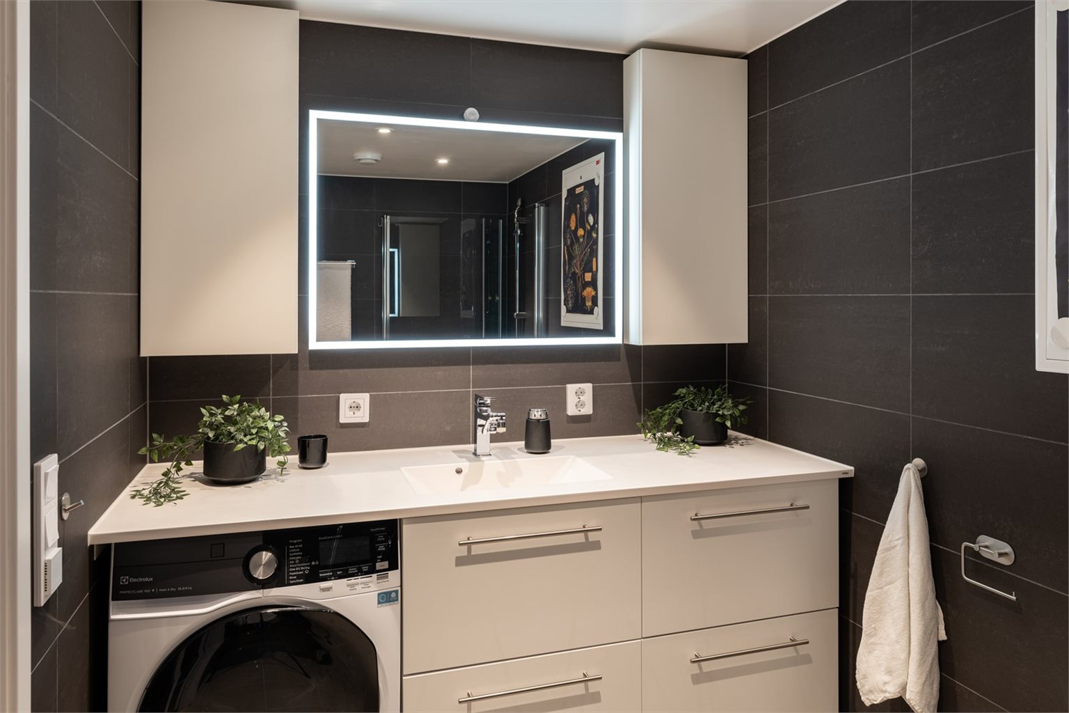 Pent og flislagt bad på 5,5m². Badet byr på servantinnredning, speil med overlys, dusjhjørne, vegghengt toalett og opplegg for vaskemaskin.