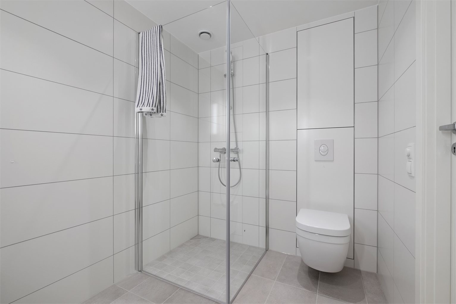 Badet er innredet med praktiske innfellbare dusjdører, opplegg for vaskemaskin, veggmontert WC- og innredet servant.
