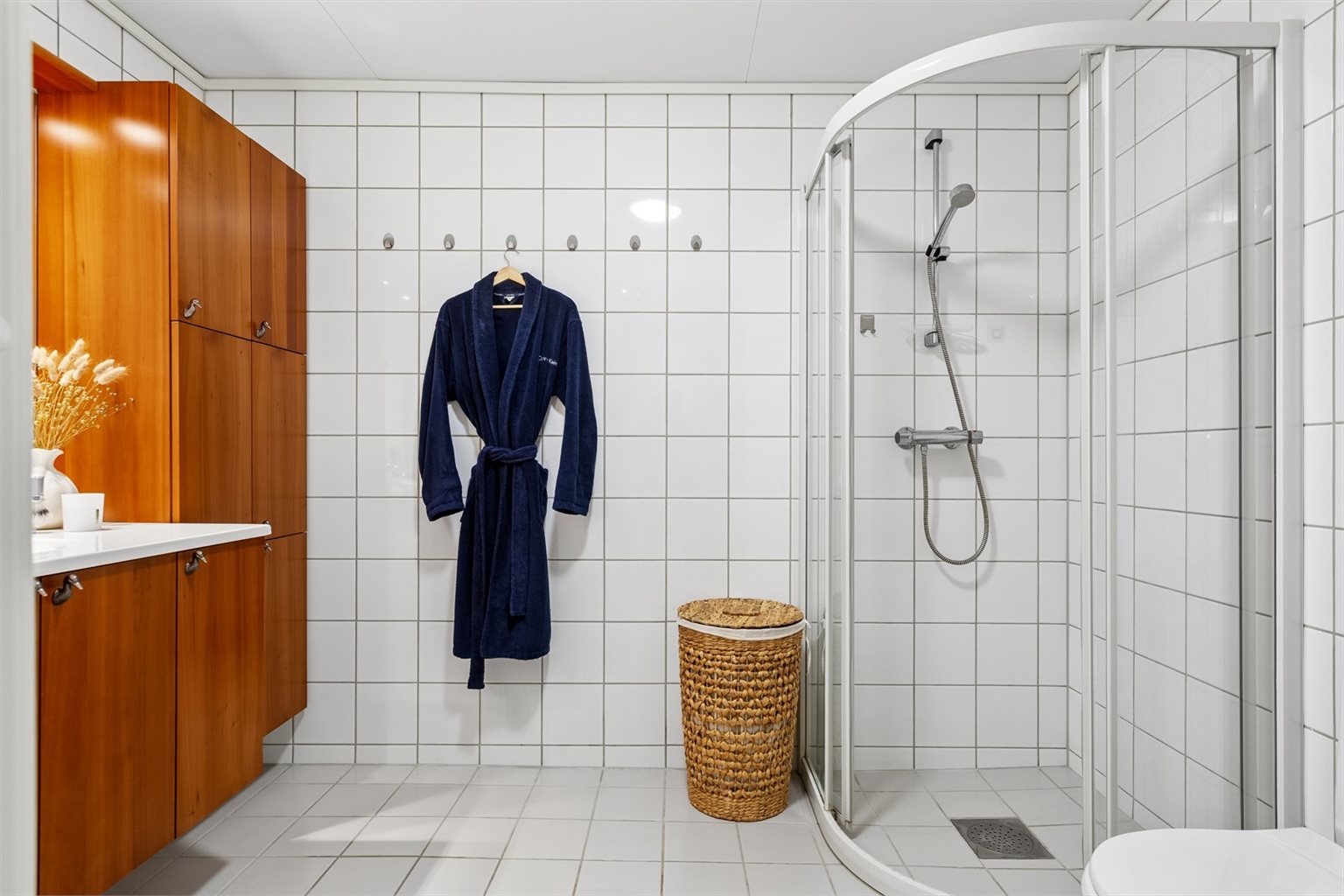 Badet har flislagte gulv og vegger som gir et tidløst og praktisk uttrykk. Det er installert gulvvarme for ekstra komfort, og himlingen er utført med takess-plater som bidrar til et pent og vedlikeholdsvennlig preg.
