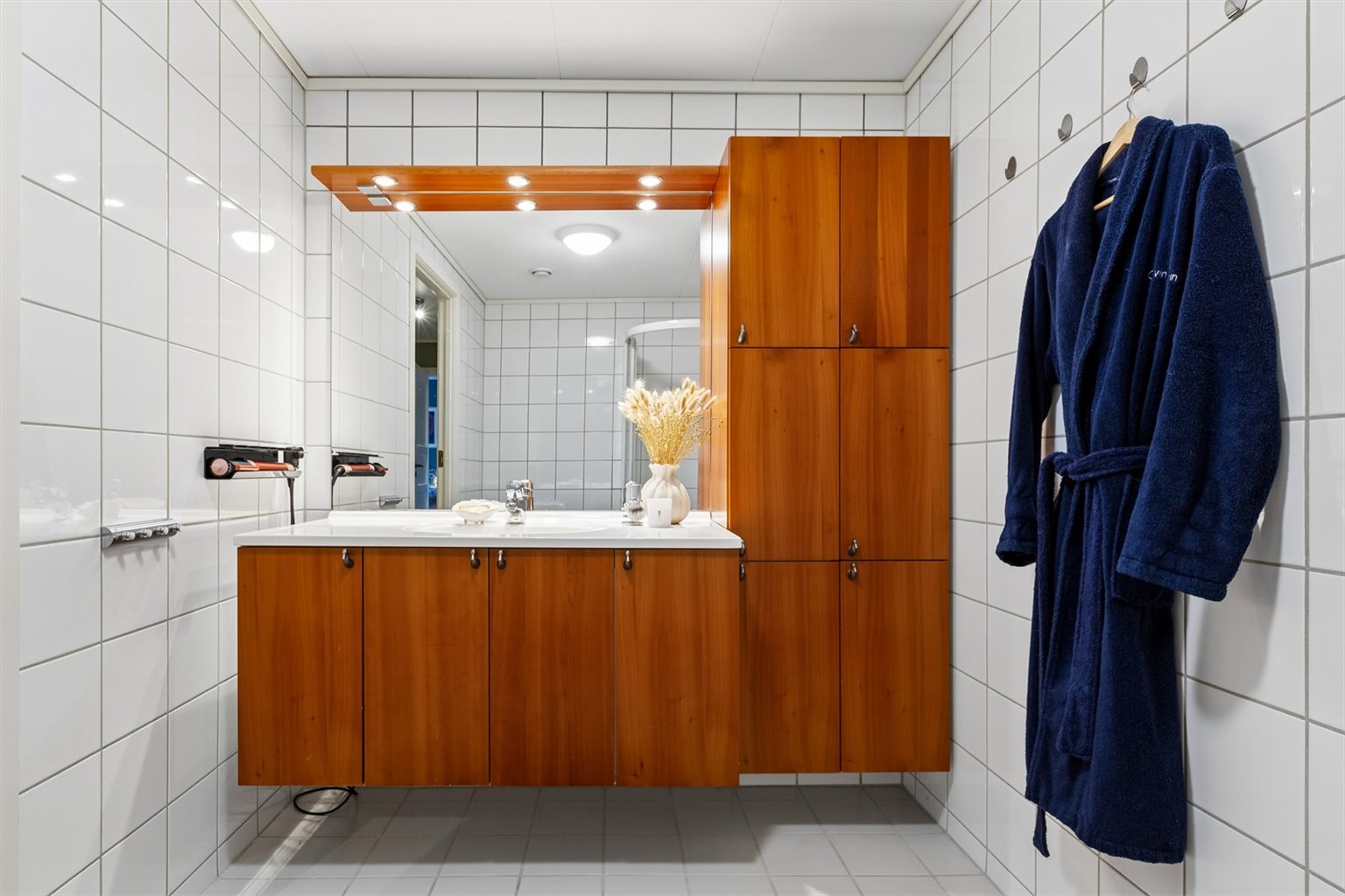 Badet har svært gode oppbevaringsmuligheter med en romslig baderomsinnredning. Et stort speil og god belysning bidrar til en lys og innbydende atmosfære, samtidig som rommet oppleves både praktisk og funksjonelt i hverdagen.