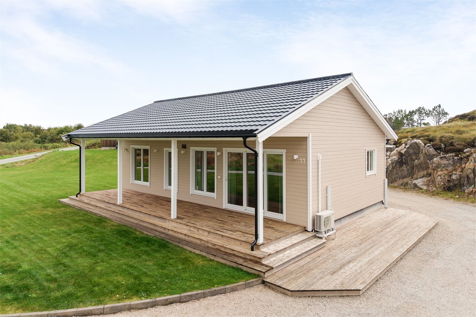 Moderne og innbydende enebolig med store vindusflater og en romslig terrasse som følger boligens fasade.