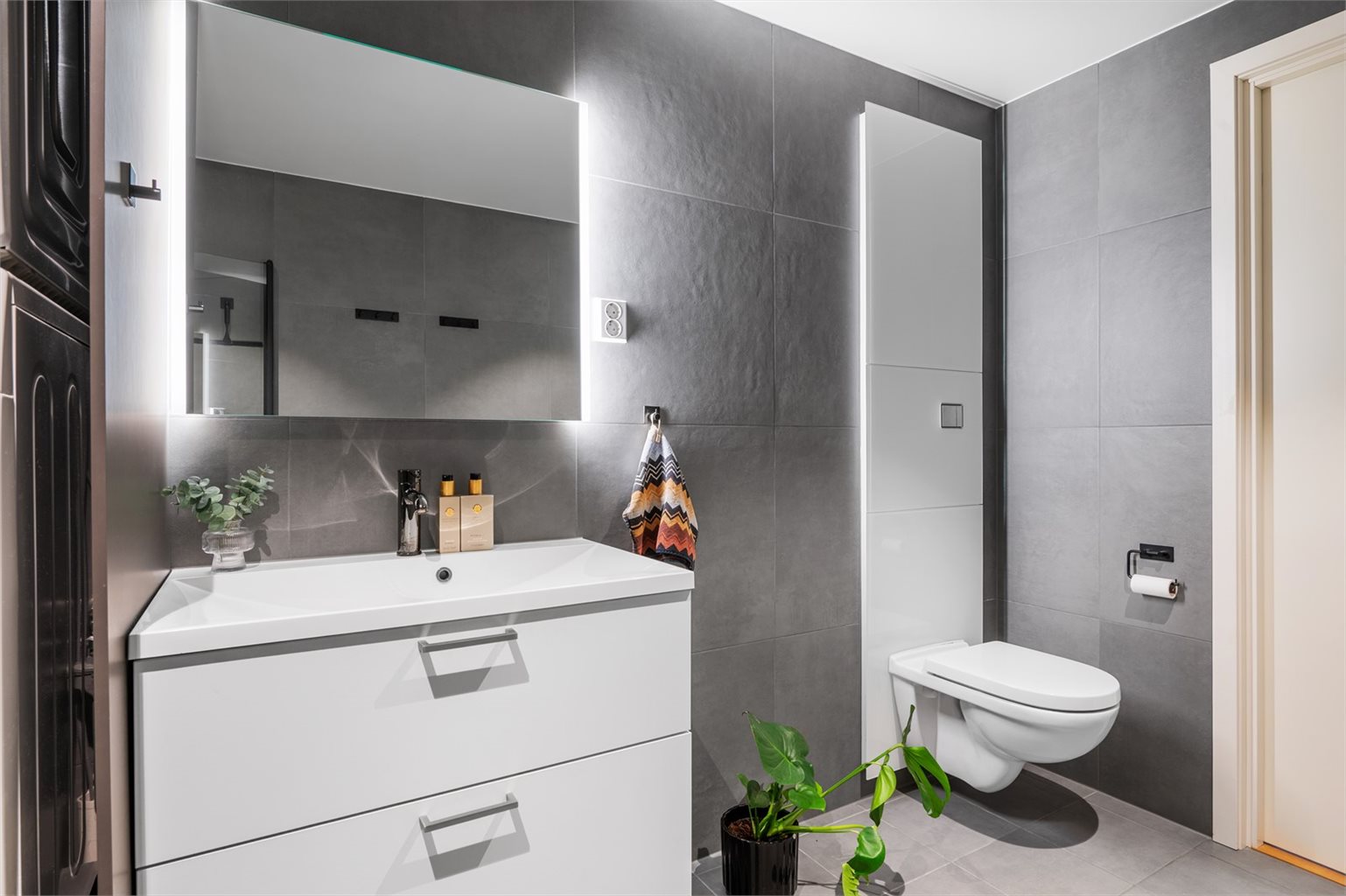 Badet er utstyrt med hjørnedusj, vegghengt toalett, baderomsinnredning samt opplegg for vaskemaskin og tørketrommel.